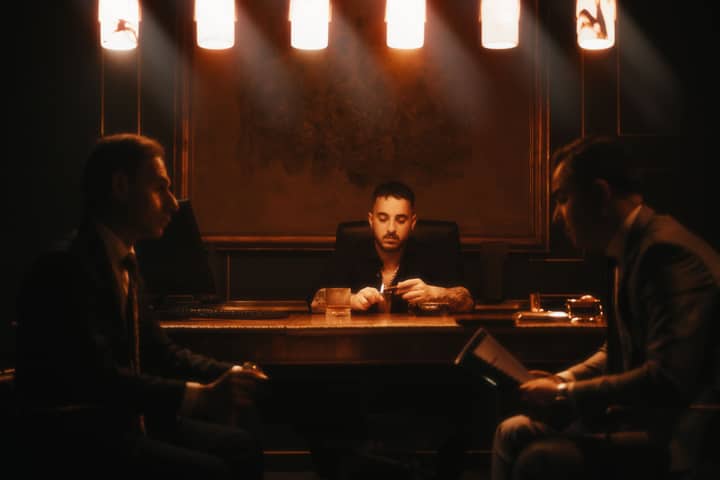 Three men in suits conduct a late-night business meeting in a dimly lit office.
