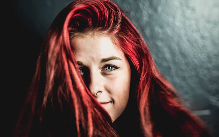 Close-up portrait of a smiling woman with striking red hair and beautiful eyes.