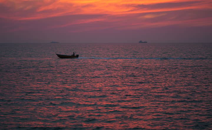 A lone boat navigates the vast ocean under a stunning red sunset sky.