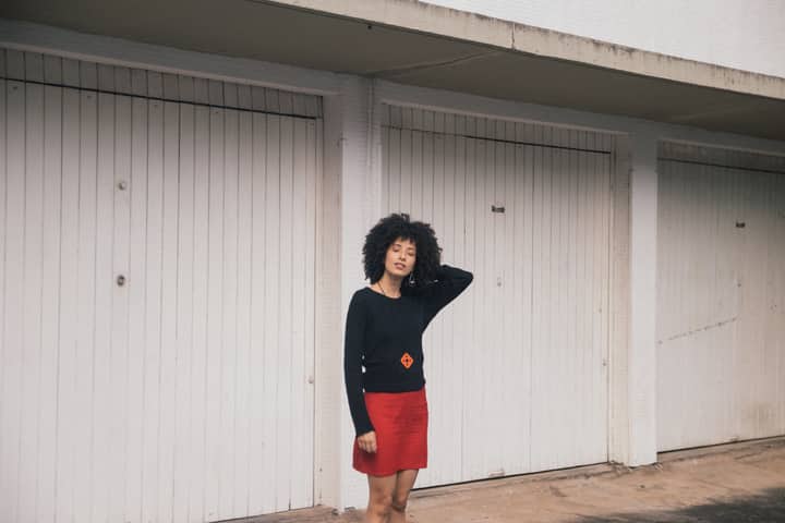 Fashionable woman in red skirt and black top posing outdoors with white garage doors in São Paulo.