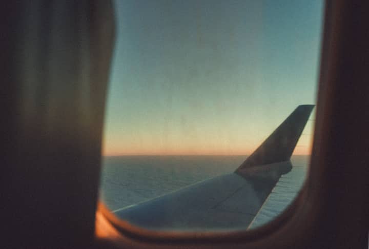 View of a sunset through an airplane wing window, flying over the sea.