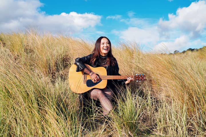 Smiling woman playing guitar in a rural landscape, enjoying the outdoors