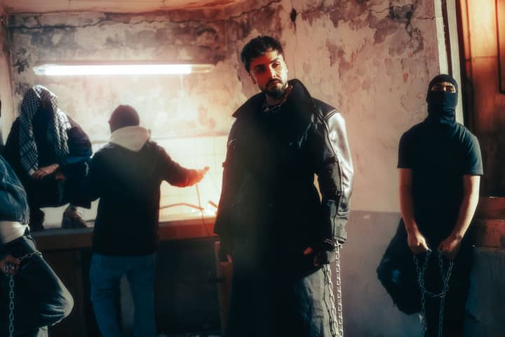 A group of men in stylish, edgy fashion in an urban setting with dramatic lighting and shadows.