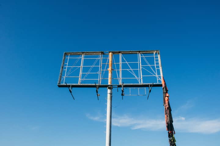 A rusty, empty billboard frame stands against a vast clear blue sky, symbolizing abandonment.