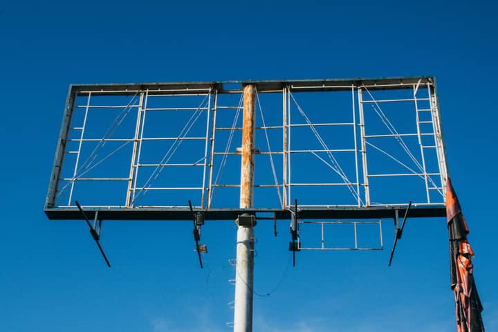 A large rusted billboard structure reaching into a clear blue sky.