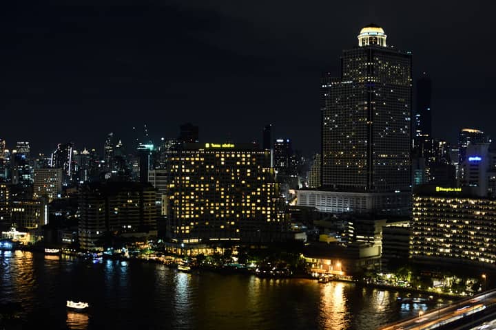 Explore the vibrant night skyline of Bangkok showcasing illuminated buildings along the riverfront, capturing the city's bustling spirit.