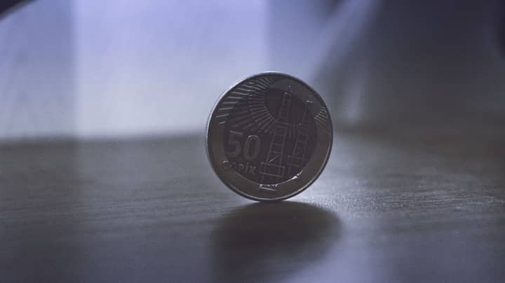 Close-up image of a 50 Qapik coin standing on a wooden surface, softly lit.