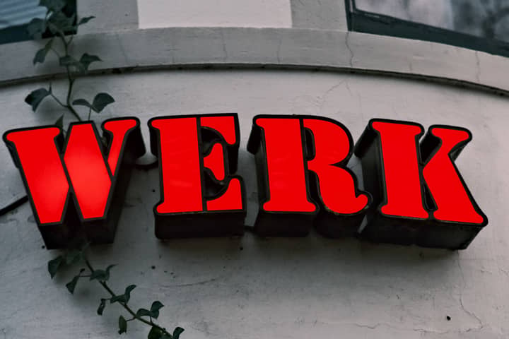 Close-up of a red 'WERK' sign on a textured wall with ivy, creating an urban vibe.