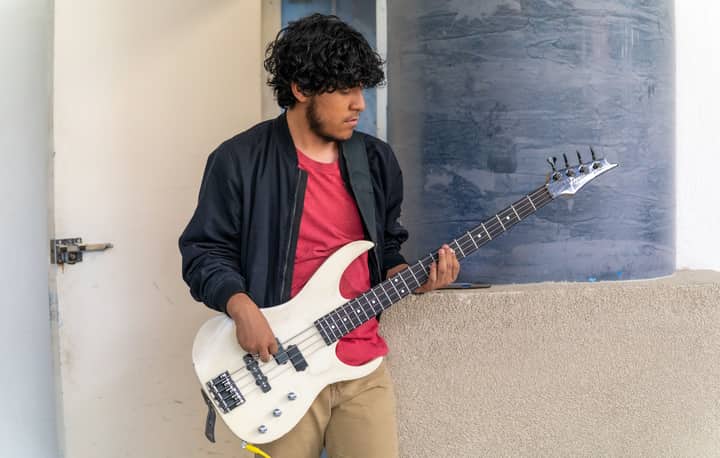 A young male musician playing an electric bass guitar outdoors in Ciudad de México.