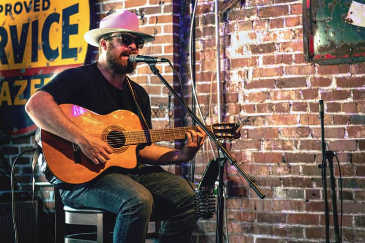 A musician plays acoustic guitar in a Nashville bar setting.