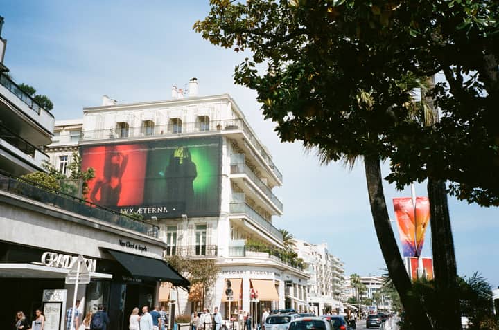 Daytime view of a bustling city street lined with luxury stores and vibrant billboards.