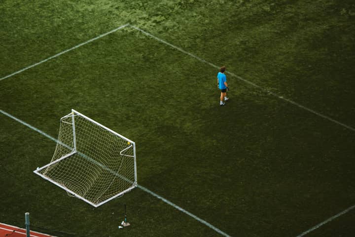 Aerial view of a lone soccer player near a goalpost on a grassy field.