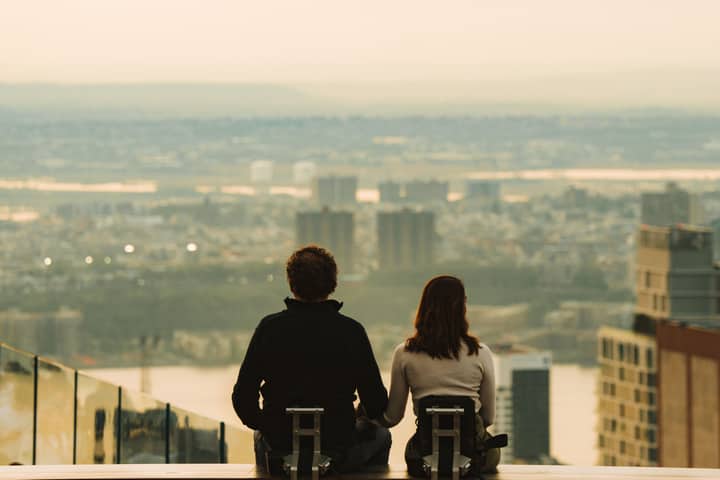A couple sits together on a rooftop, enjoying a panoramic view of the city skyline, creating a romantic urban moment.