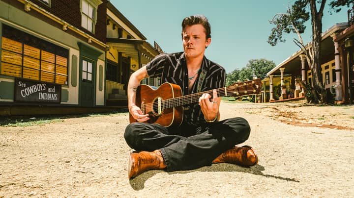 Musician seated with guitar in a rustic Western-themed town, Wimberley, TX