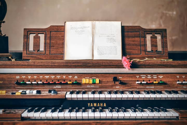 Close-up of a vintage Yamaha organ with sheet music and a pink flower, perfect for musical nostalgia.