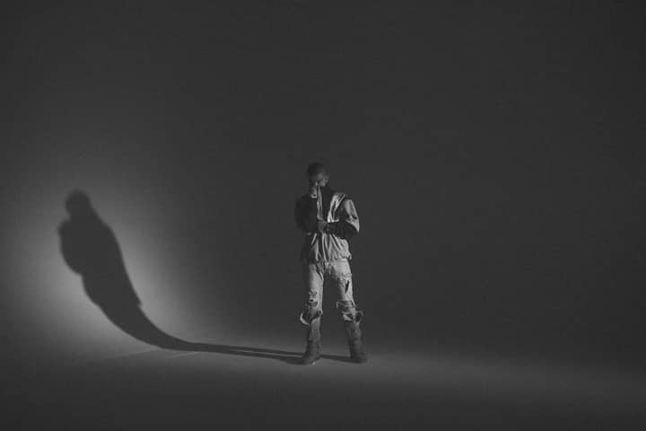 A monochrome portrait of a man in a studio setting, featuring bold shadows and casual fashion.