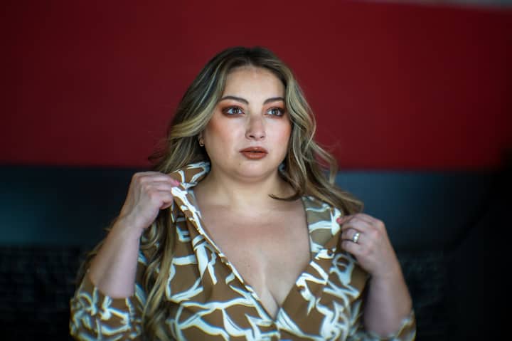 Adult woman confidently posing indoors with elegant hairstyle and makeup, wearing a stylish patterned shirt.