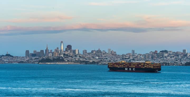 A panoramic view of San Francisco's skyline with a cargo ship on the bay at dusk.