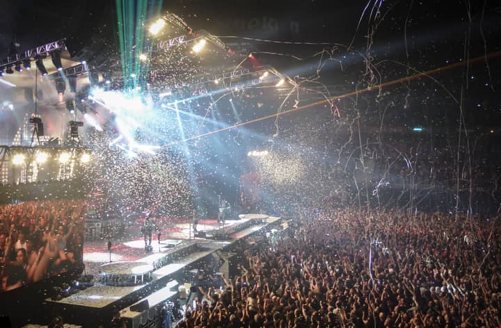Vibrant concert scene with dynamic lighting, confetti, and a large enthusiastic crowd.