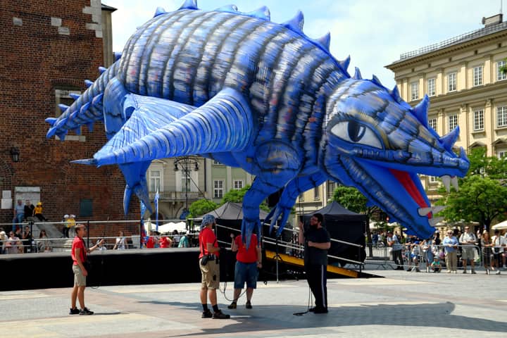 Large blue dragon balloon displayed outdoors in a lively summer parade setting.