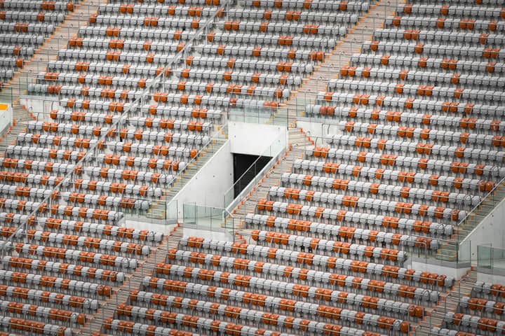 An aerial view of a modern stadium with orange and gray seats forming geometric patterns.