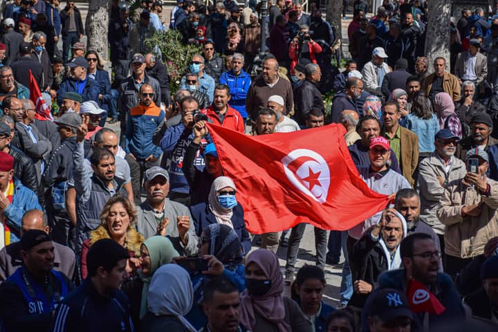 Crowd gathered in Tunis holding the Tunisian flag during a daytime demonstration.