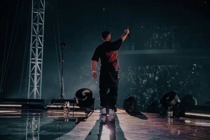 An energetic rapper performing on stage in Tirana, with a vibrant crowd and powerful stage lights.