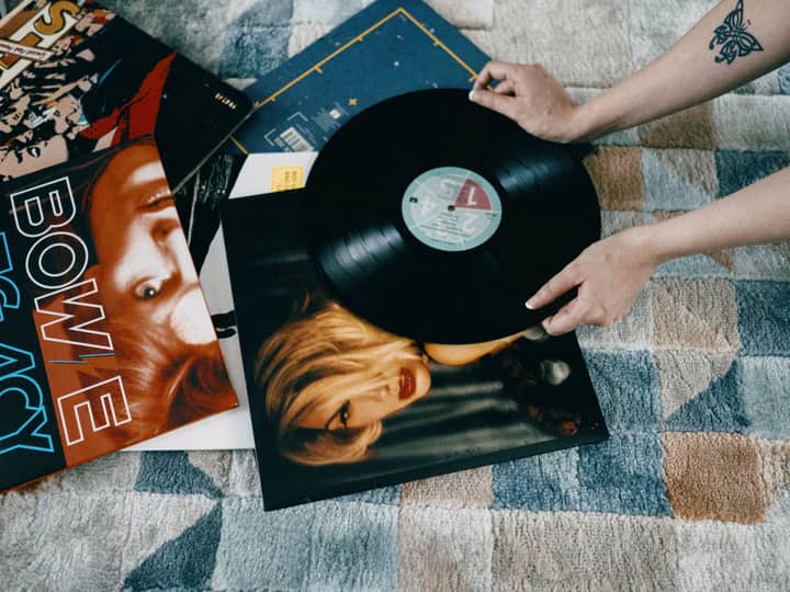 Hands holding a vinyl record above album covers, showcasing a love for music and nostalgia.