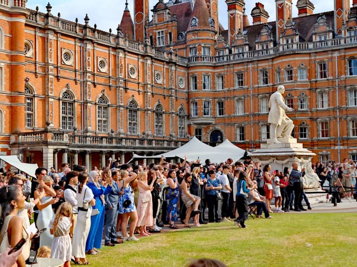 A large crowd gathers for a graduation ceremony at a historic university in England, featuring ornate architecture.