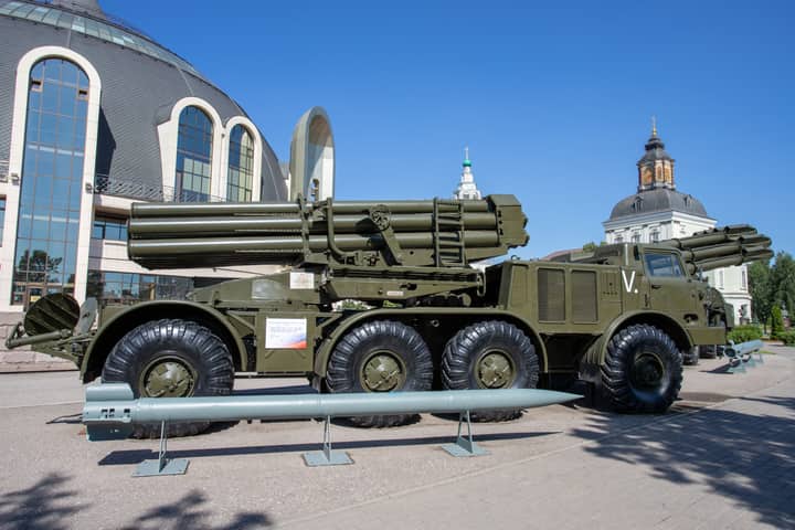 A military missile launcher on exhibit outdoors with a backdrop of unique architecture and clear blue sky.