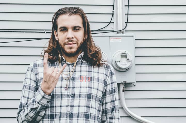 Young man with long hair making rock gesture in front of a wall in Chicago.