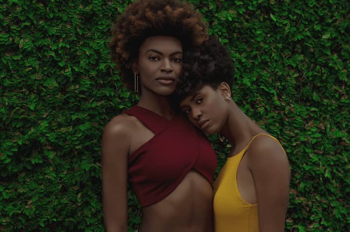 Stylish portrait of African American women in vibrant outfits against a leafy background.