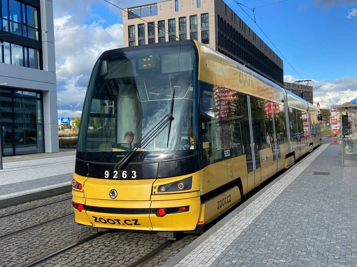 Yellow tram in urban Prague, showcasing public transit near modern architecture.