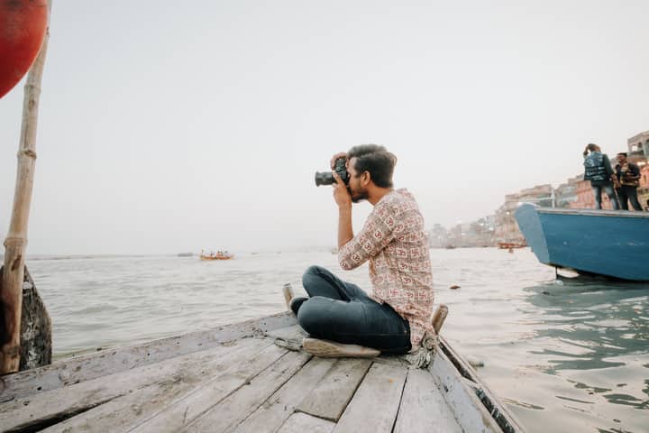 A man taking photos while seated on a boat by the water, capturing scenic views and enjoying leisurely travel.