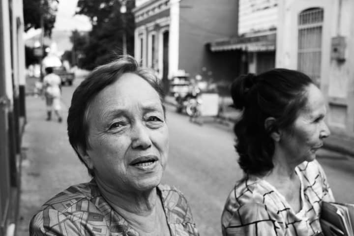 A candid portrait of two elderly women interacting on a street in Zulia, Venezuela. Black and white.