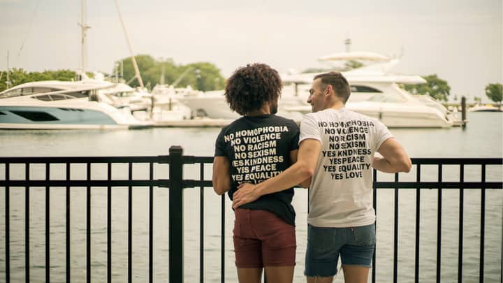 Couple embracing by the marina wearing T-shirts promoting love and equality.