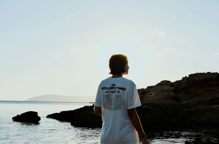 Silhouette of a person by the rocky seashore during sunset, serene ocean view.