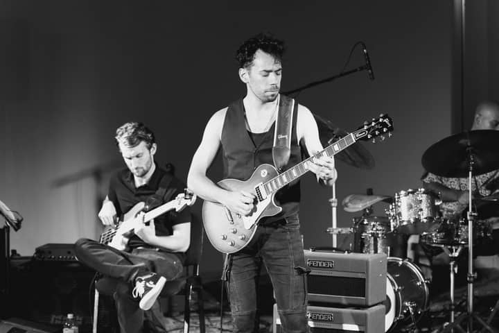 Black and white image capturing a live music band performance with guitar and drum solo.