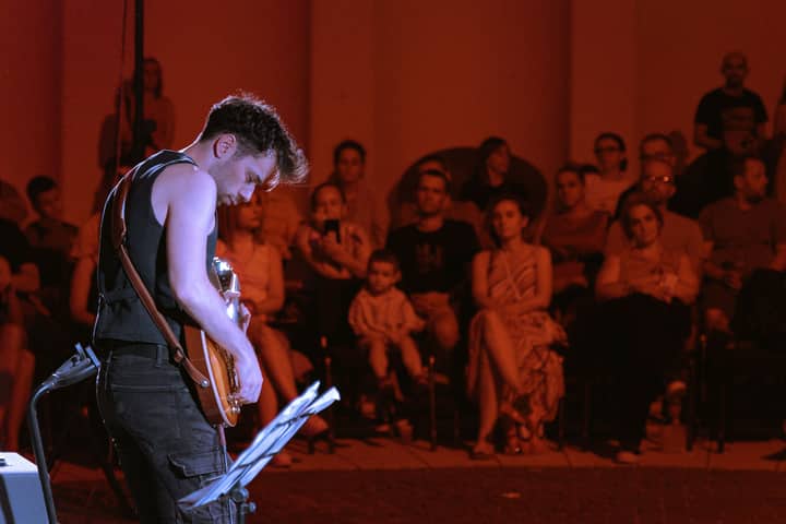 Guitarist performs live on stage under warm lights with a captivated audience.