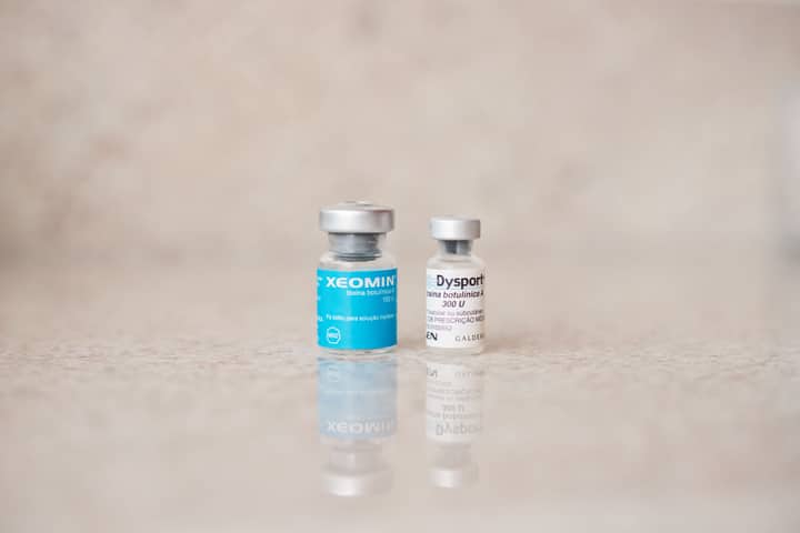 Close-up of Xeomin and Dysport bottles reflecting on a surface, shot indoors.
