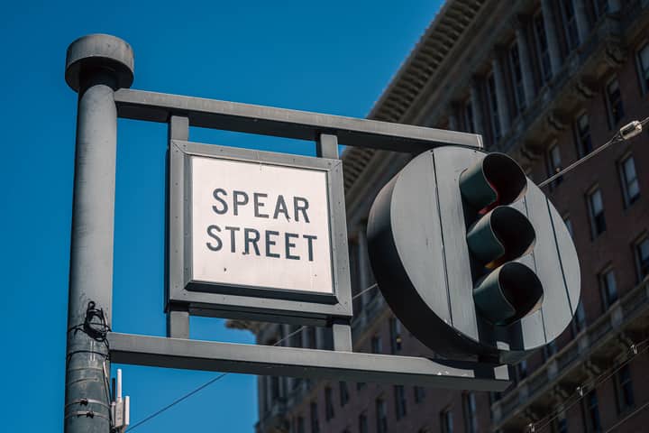 Traffic light and Spear Street sign with urban building backdrop in daylight.