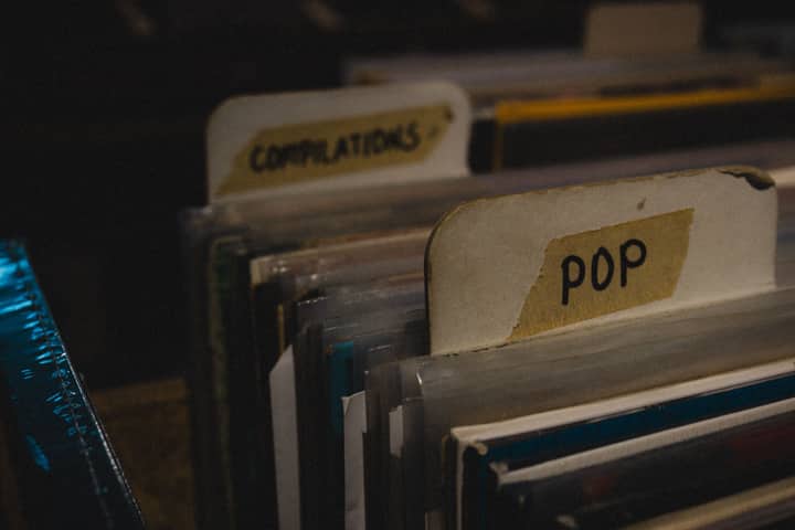 A close-up of vinyl records categorized under 'POP' and 'COMPILATIONS' in a dimly lit retro store.
