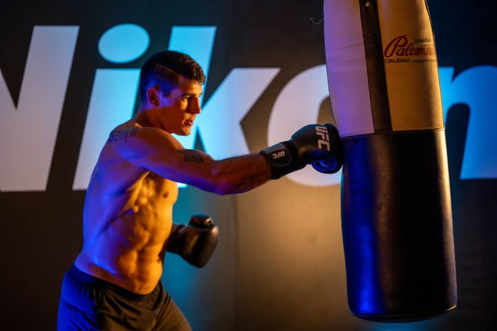 A male boxer trains intensely with a punching bag indoors at a gym in Mexico City.