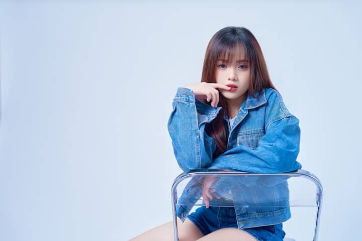 Studio portrait of a young woman in a denim jacket posing stylishly.