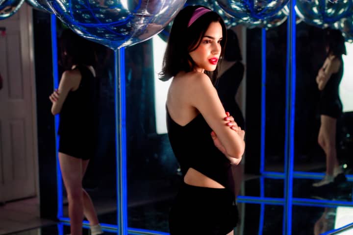 A fashionable woman posing with confidence in a vibrant, reflective nightclub setting.