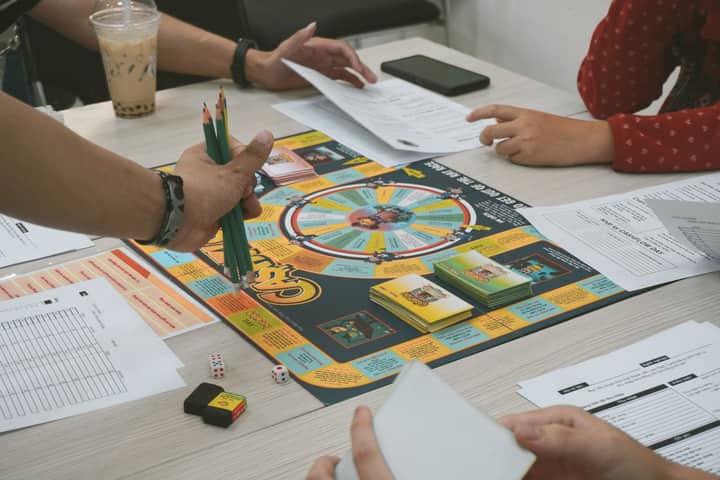 A group of adults playing the Cashflow board game, concentrating on financial planning.