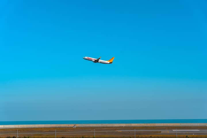 An airplane takes off from an airport runway, soaring into the clear blue sky over the ocean.