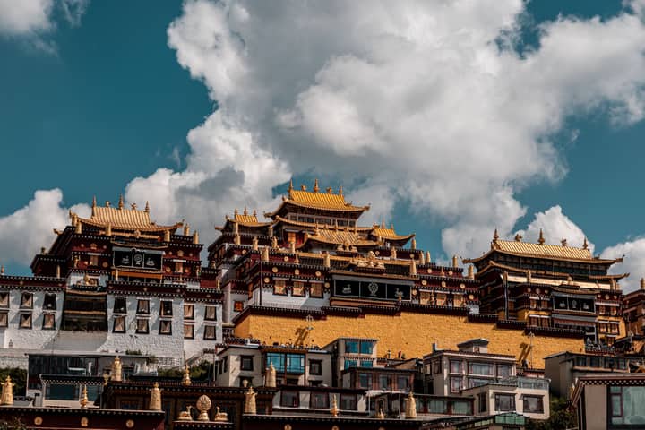 Majestic Buddhist temple complex with ornate architecture under a vibrant blue sky and clouds.