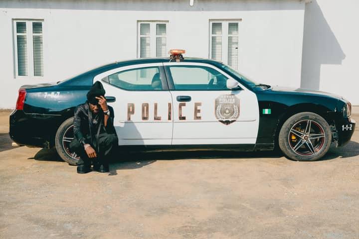 Police officer seated by car in urban area during the day.