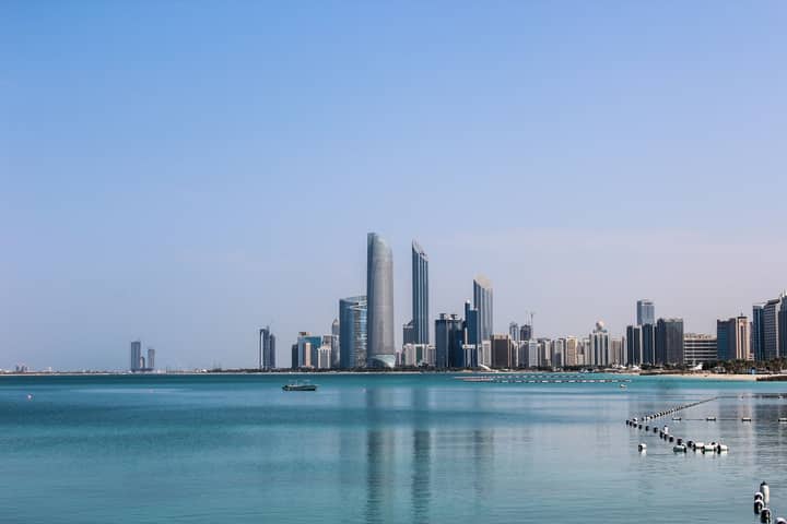 Stunning view of the Abu Dhabi skyline reflecting in the calm Gulf waters on a sunny day.